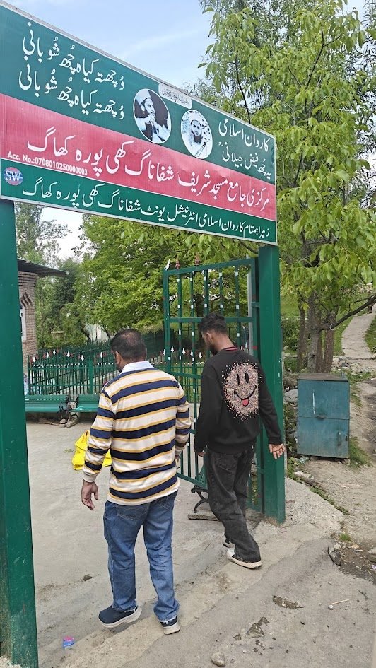 Green gate entrance to the Sitaharan shrine with Urdu text signage, two men walking through