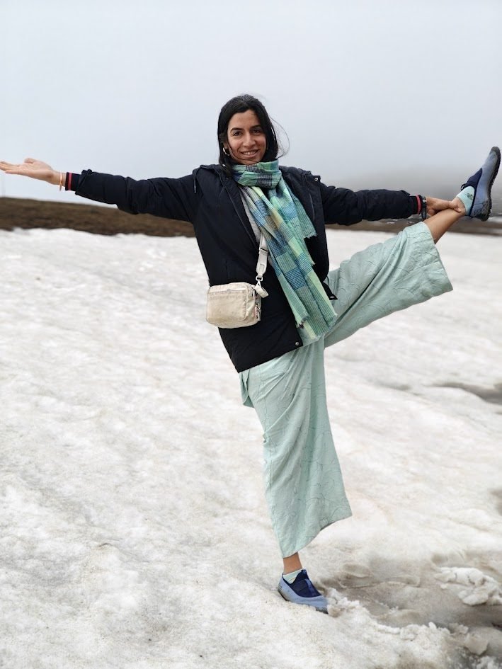 Varuna Shunglu doing a dancer balance pose on a snowfield in Kashmir with mist and mountains behind her