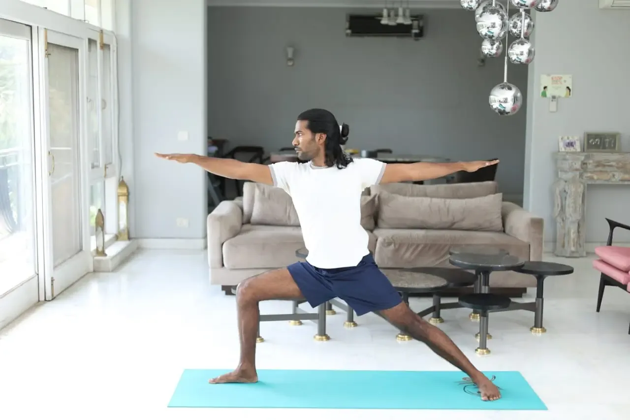 A man practicing Warrior 2 yoga pose in a calm, quiet indoor space